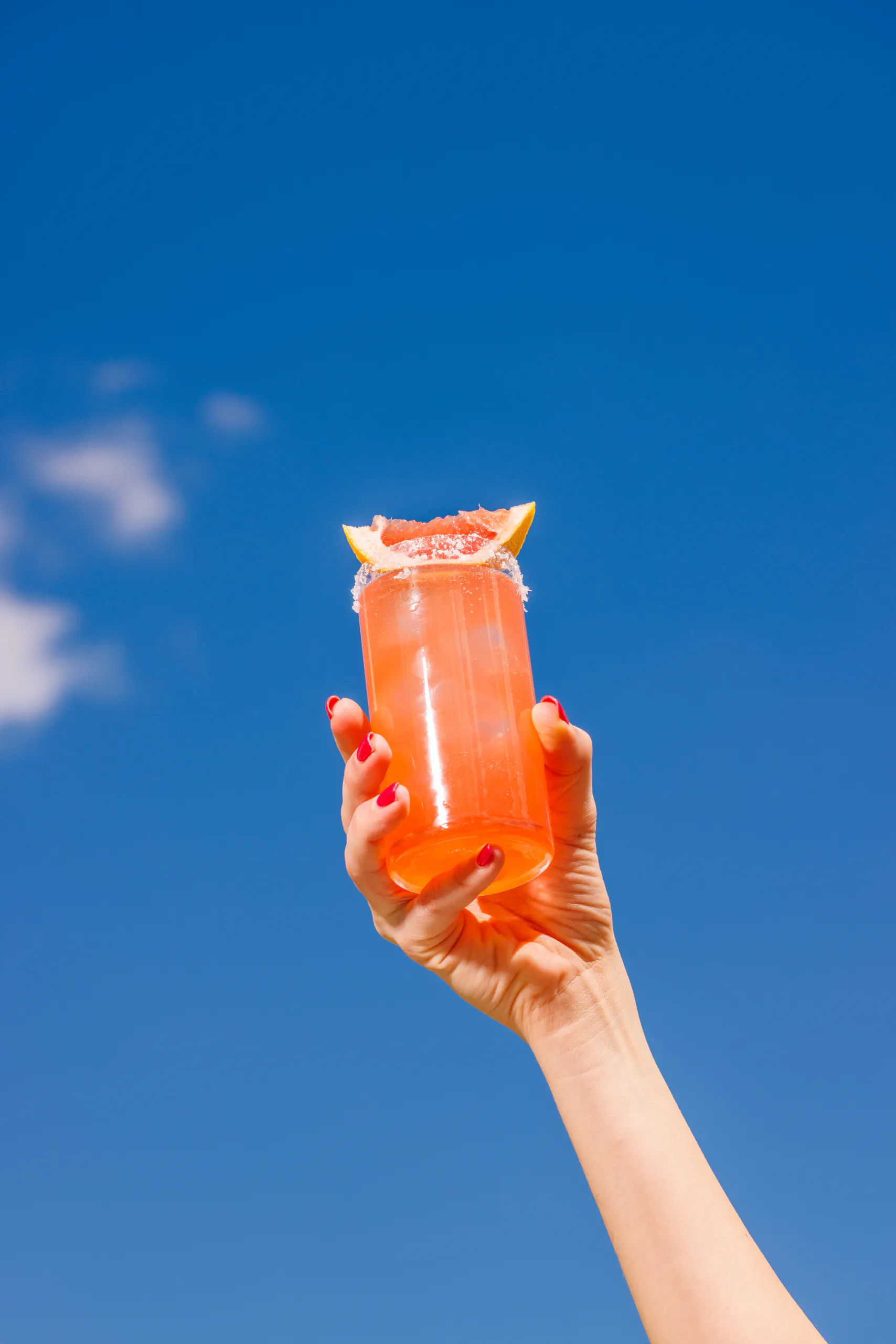 Hand holding up an orange cocktail against a blue sky