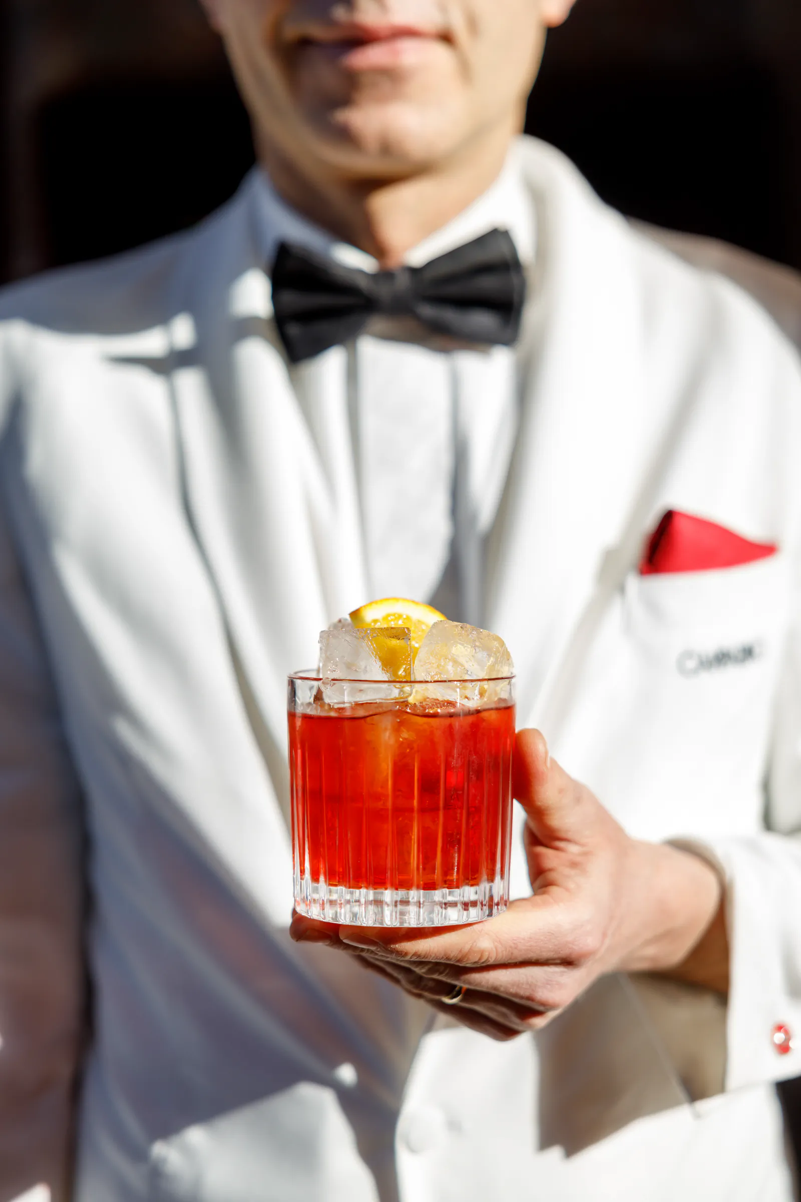 Man in a white tuxedo holding a negroni garnished with orange peel at Camparino in galleria, Milan, Italy