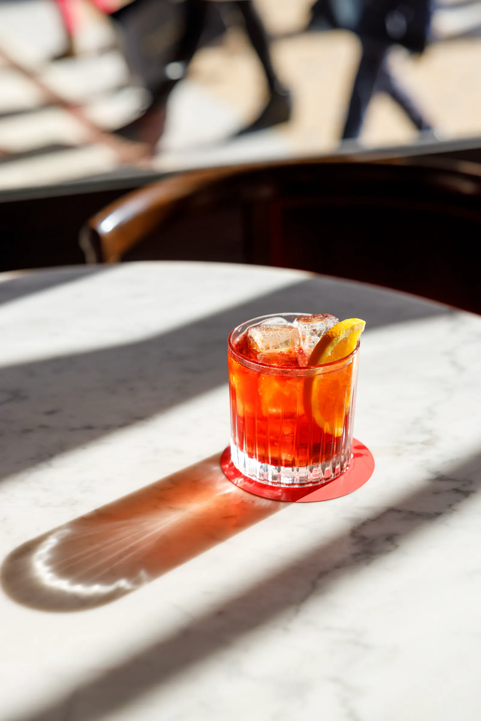Negroni with orange peel in a rocks glass on a sunlit marble cafe table at Camparino in galleria, Milan, Italy