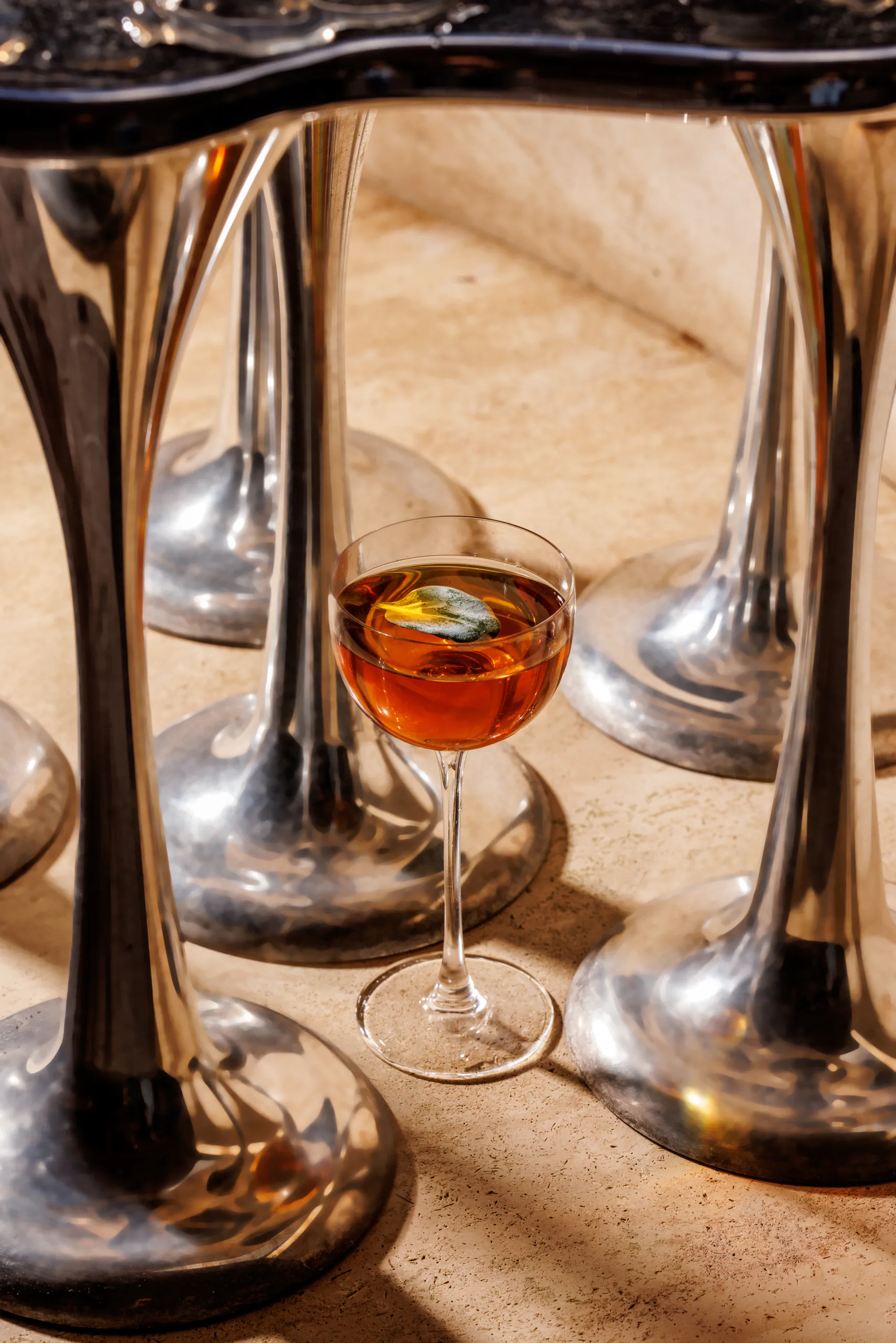 Amber cocktail among upturned cocktail tins on a sunlit textured surface
