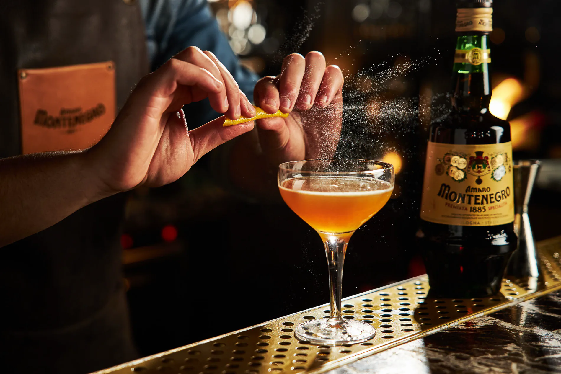 Bartender expressing citrus peel over a cocktail beside an Amaro Montenegro bottle