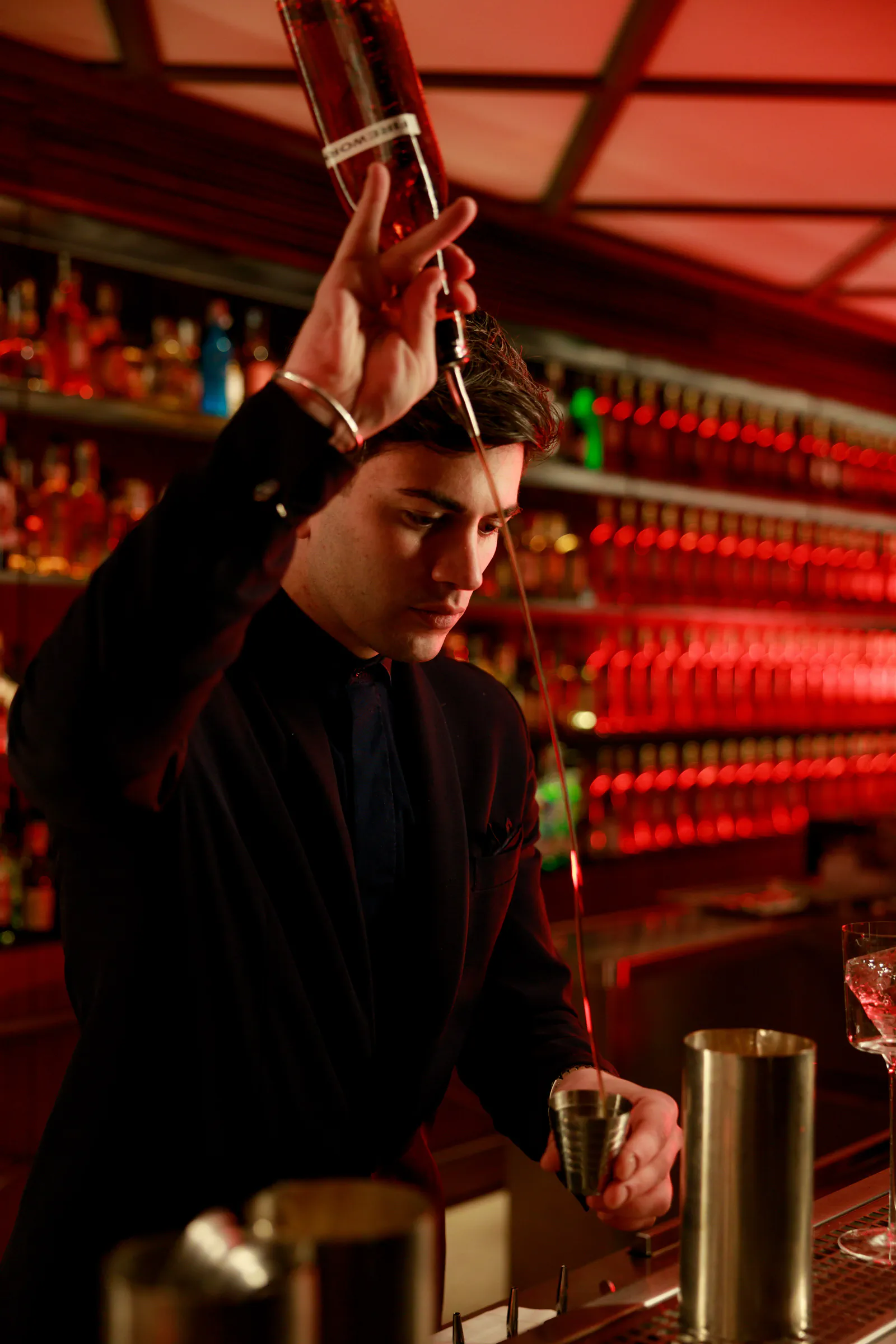 Bartender shaking a cocktail with the shaker held high at a red-lit bar — Camparino in Galleria, Milan