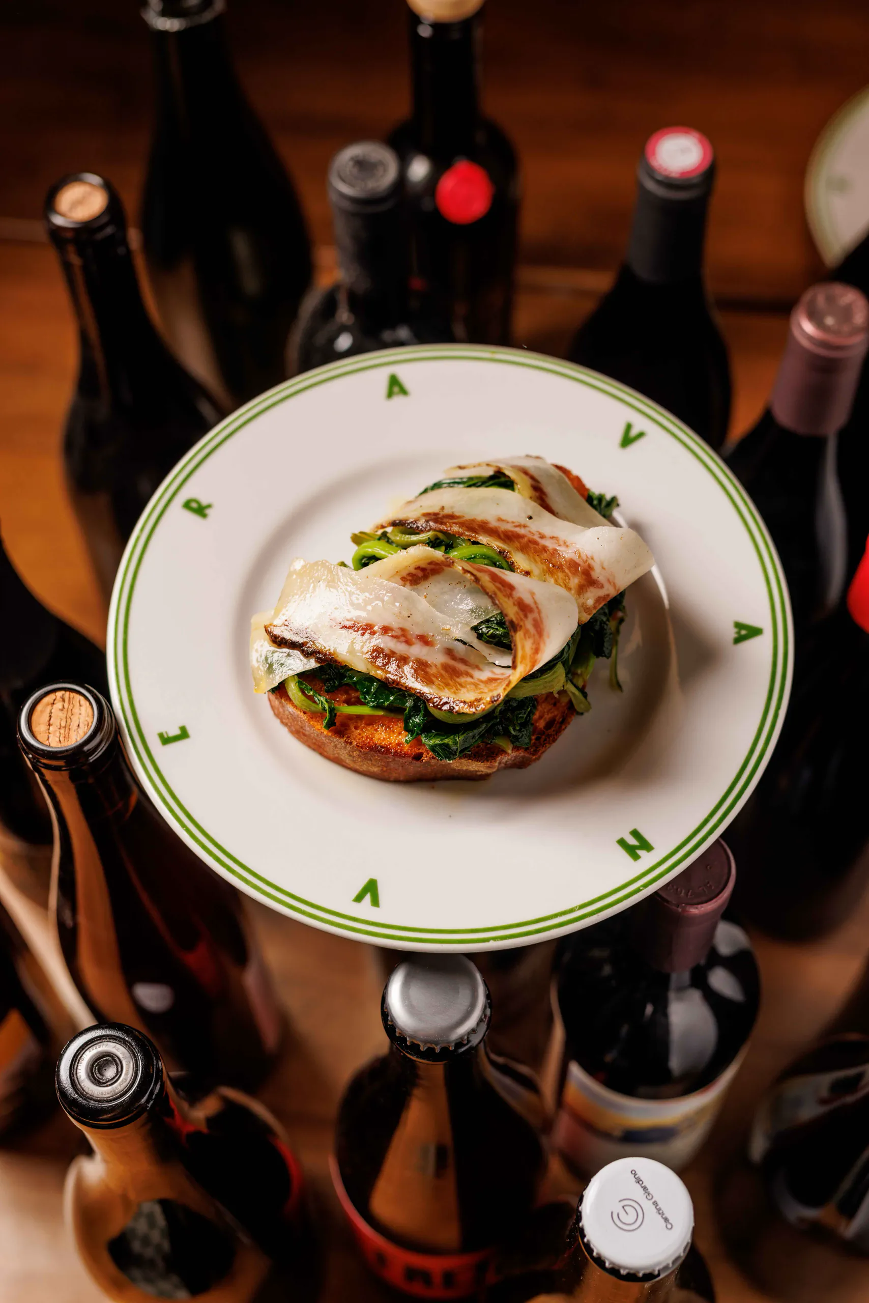 Rolled fish over greens on a green-rimmed plate framed by wine bottles - Avanvera, Rome, Italy