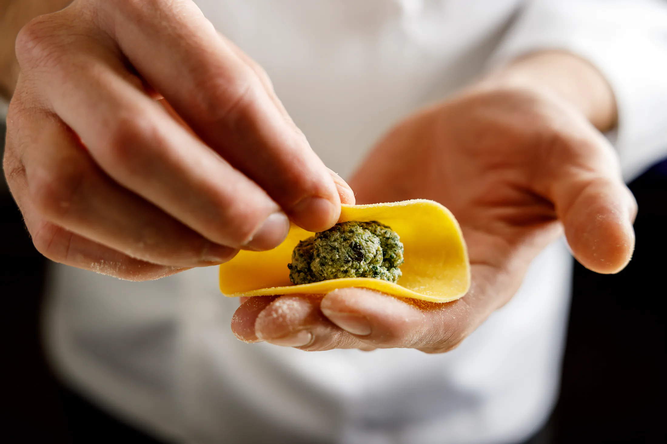 Hands filling fresh pasta with a green stuffing