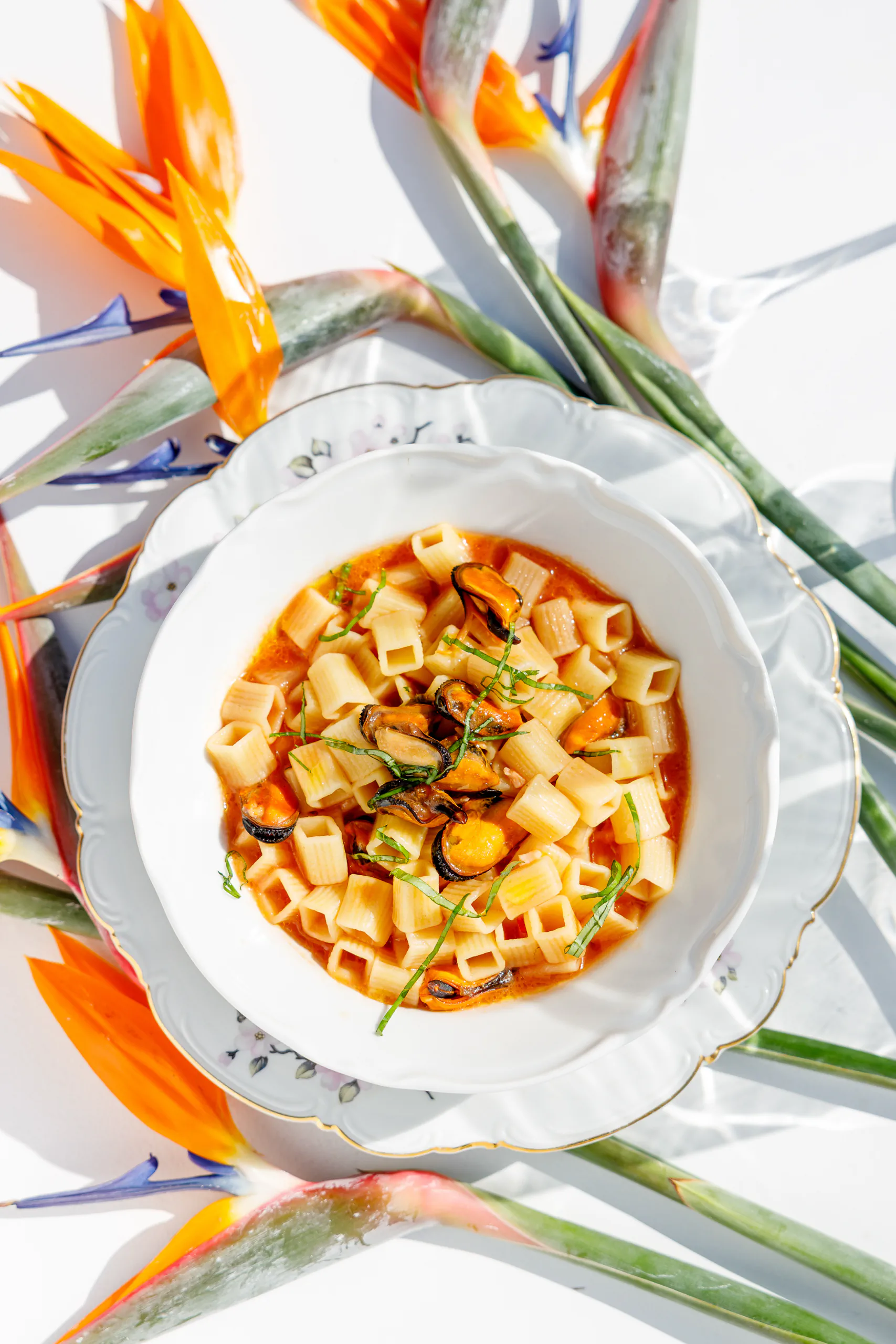 Seafood pasta soup framed by bird-of-paradise flowers - Bianca Restaurant, Santa Marinella, Italy