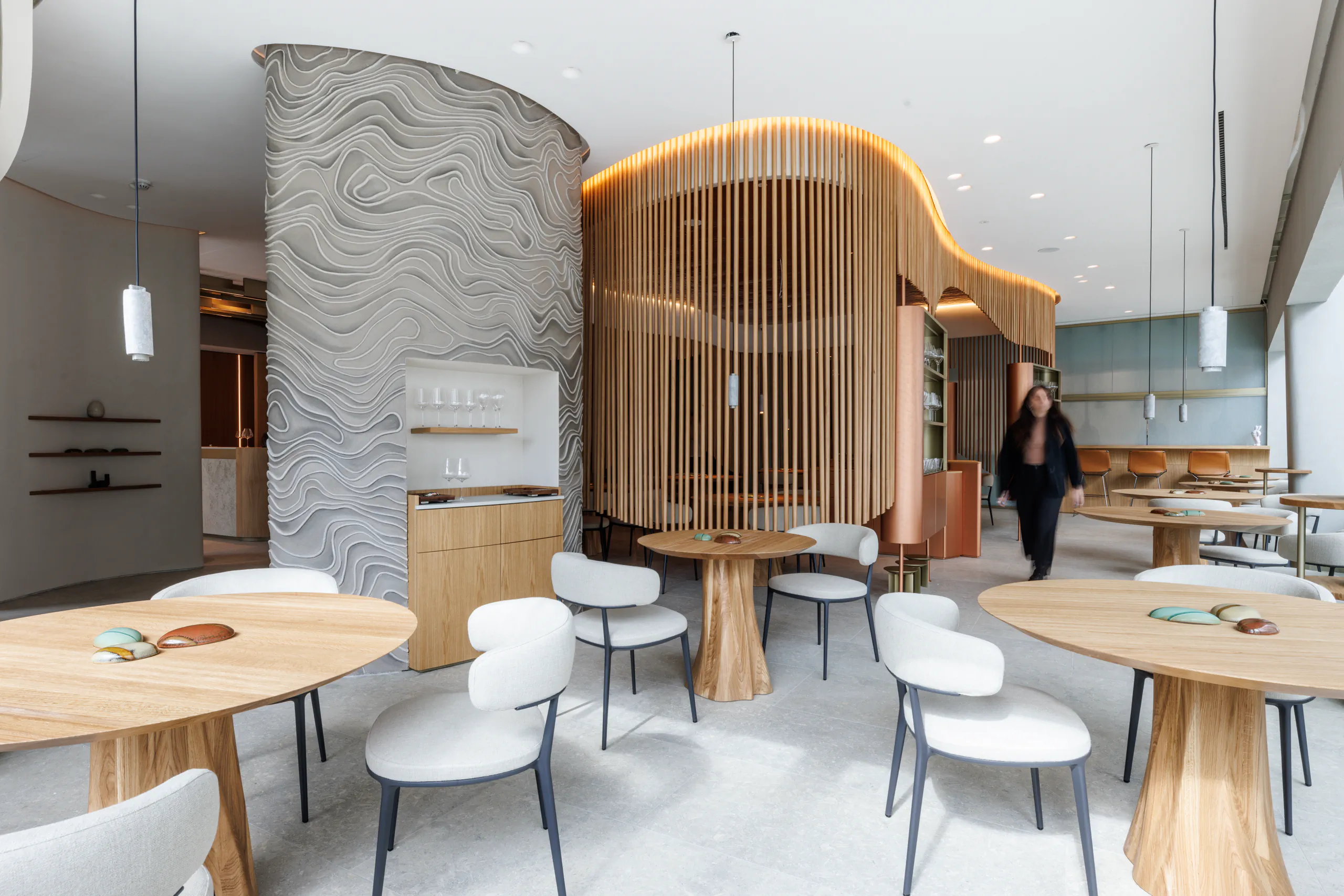 Modern dining room with round wooden tables, white chairs and a curved wooden partition