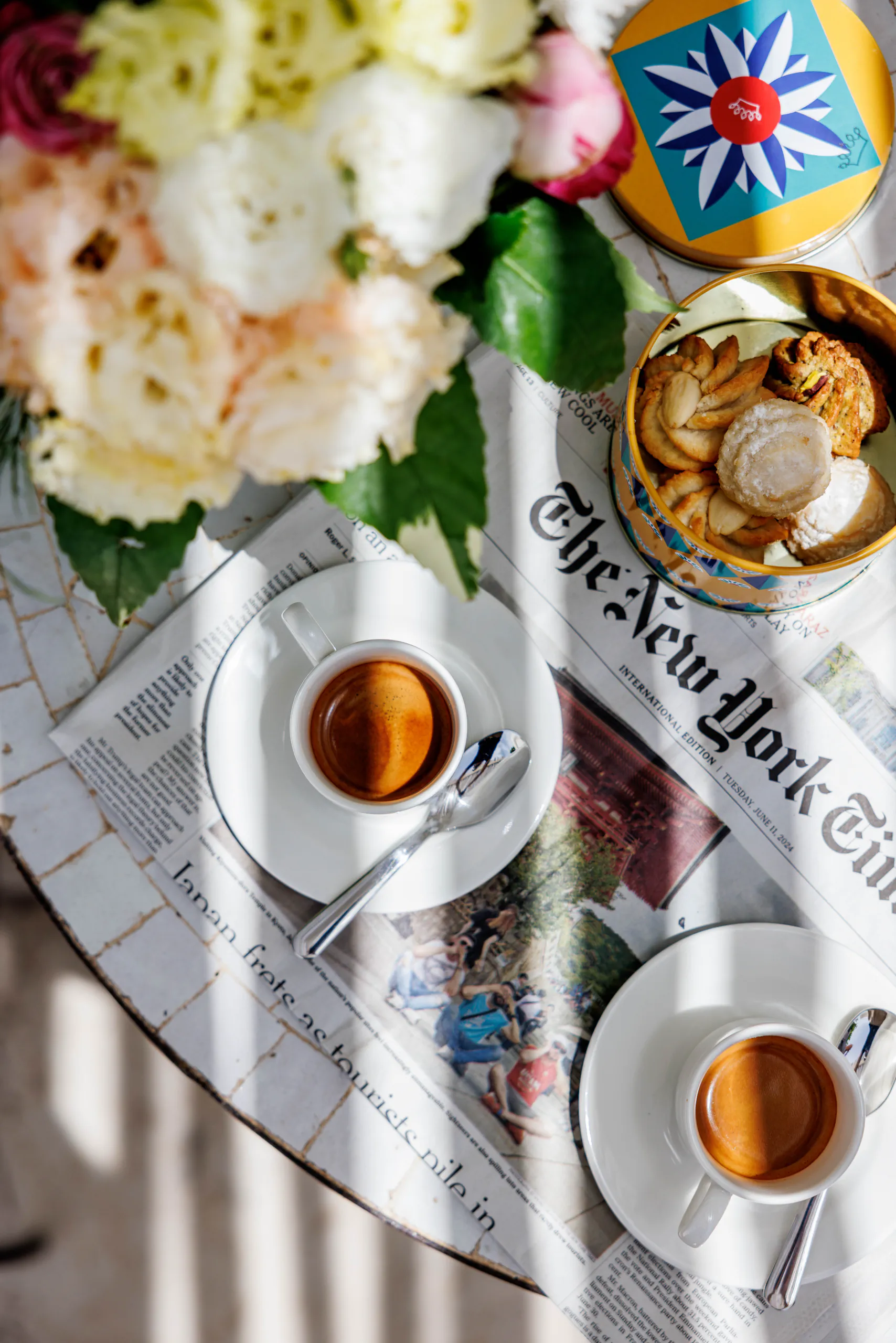 Overhead breakfast with espresso, pastries, flowers and a newspaper