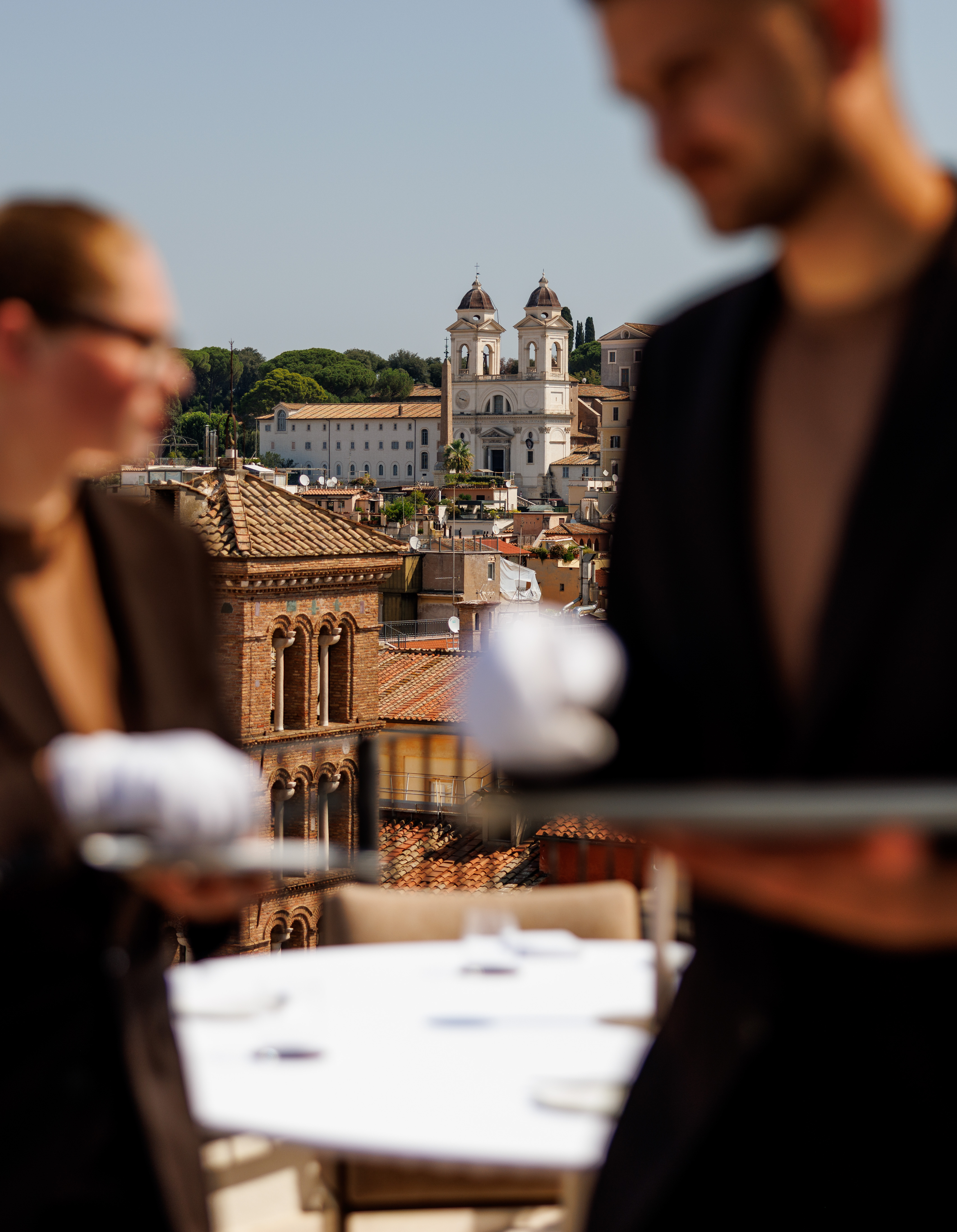 Waiters carrying trays on a rooftop terrace overlooking Rome